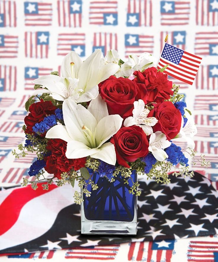 red, white and blue flowers in a vase on a table with an american flag background