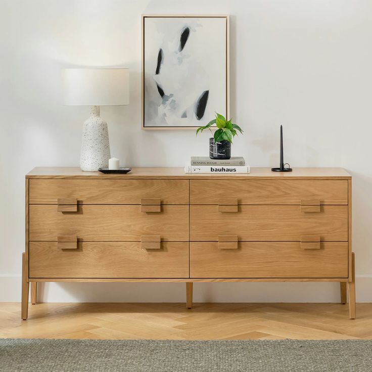 a wooden dresser with two lamps and a painting on the wall