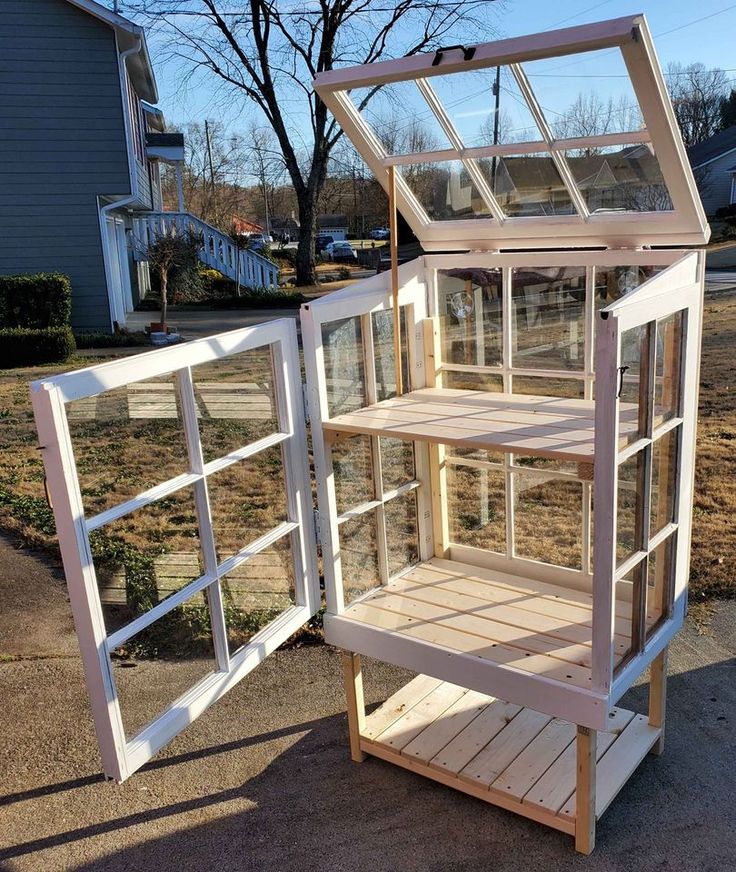 a wooden shelf with glass doors on the top and bottom shelves, in front of a house