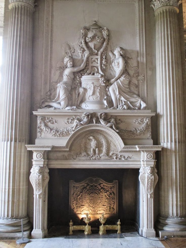 an ornate fireplace in the middle of a room with columns and statues on it's sides