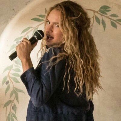 a woman singing into a microphone in front of a wall with leaves painted on it