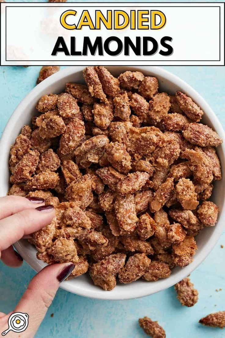 a bowl filled with candied almonds on top of a blue table next to a hand