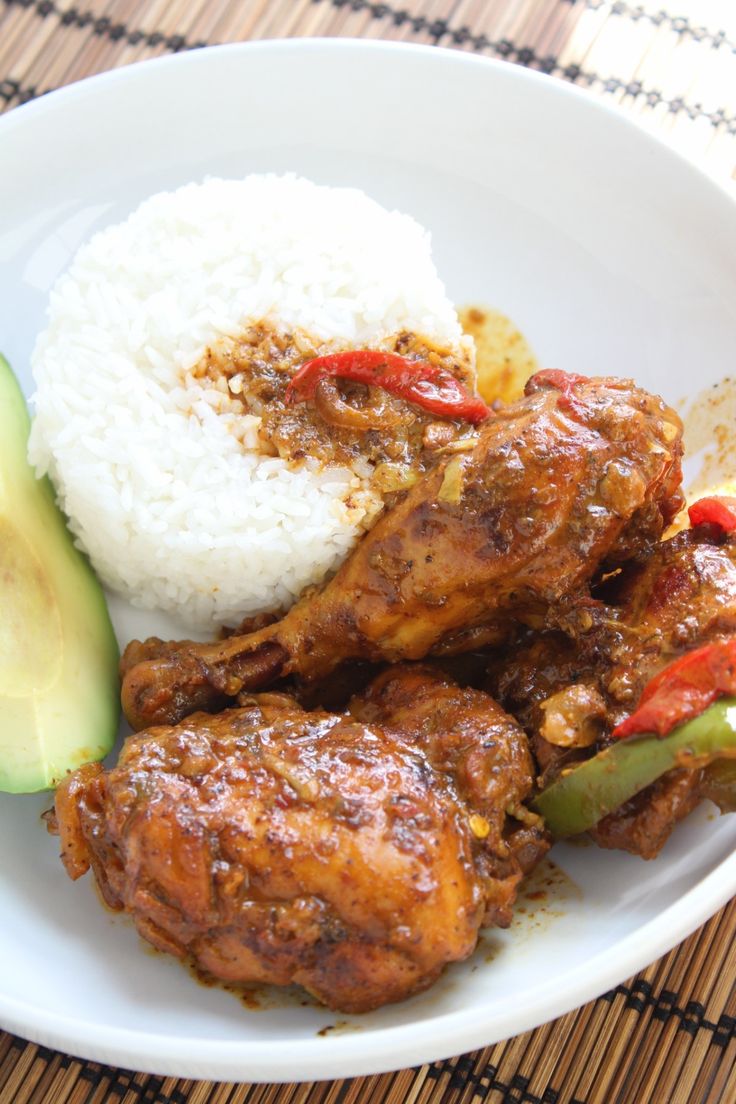 a white plate topped with meat and rice next to an avocado slice on top of a table