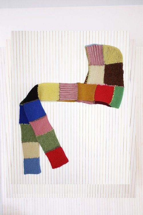 a colorful knitted scarf hanging on the wall in front of a white striped wall