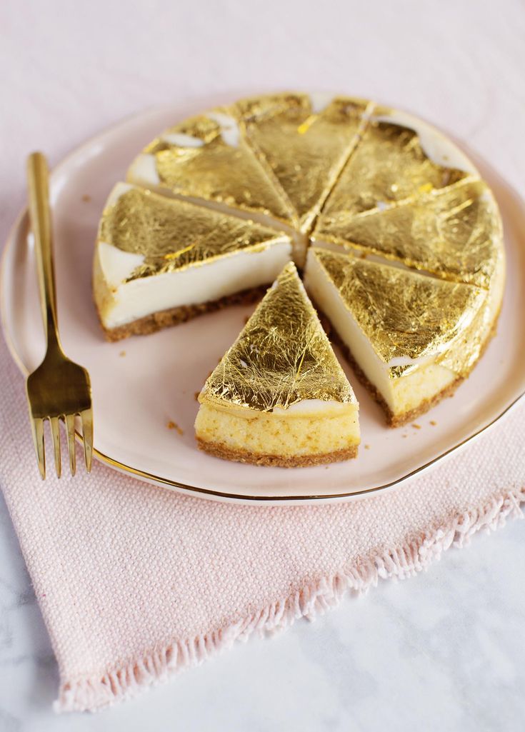 a piece of cheesecake on a pink plate with a gold fork next to it