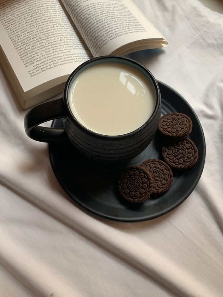 a cup of milk and cookies on a plate with an open book next to it