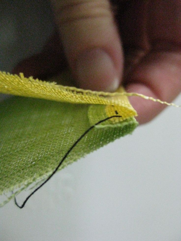 someone is stitching the end of a green piece of cloth with thread on it