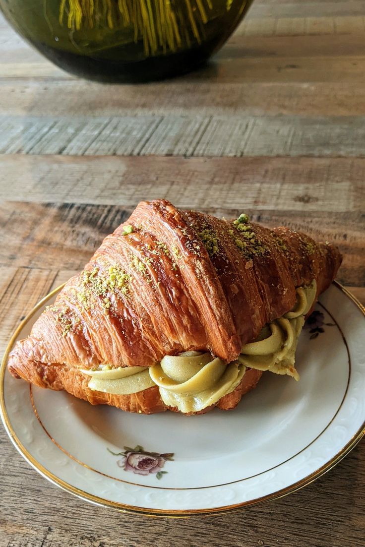 a croissant sandwich on a white plate with yellow sauce and sprinkles