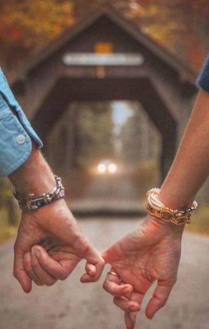 two people holding hands while walking down a road