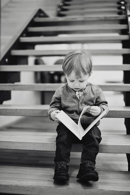 a little boy sitting on top of a wooden bench holding a book in his hands