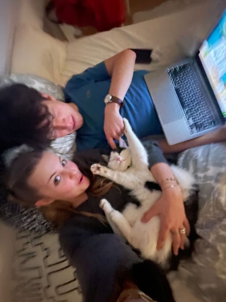 two people laying on a bed with a cat