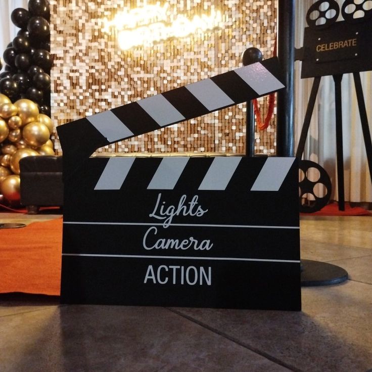 a black clapper sitting on top of a floor next to a golden ball and some balloons