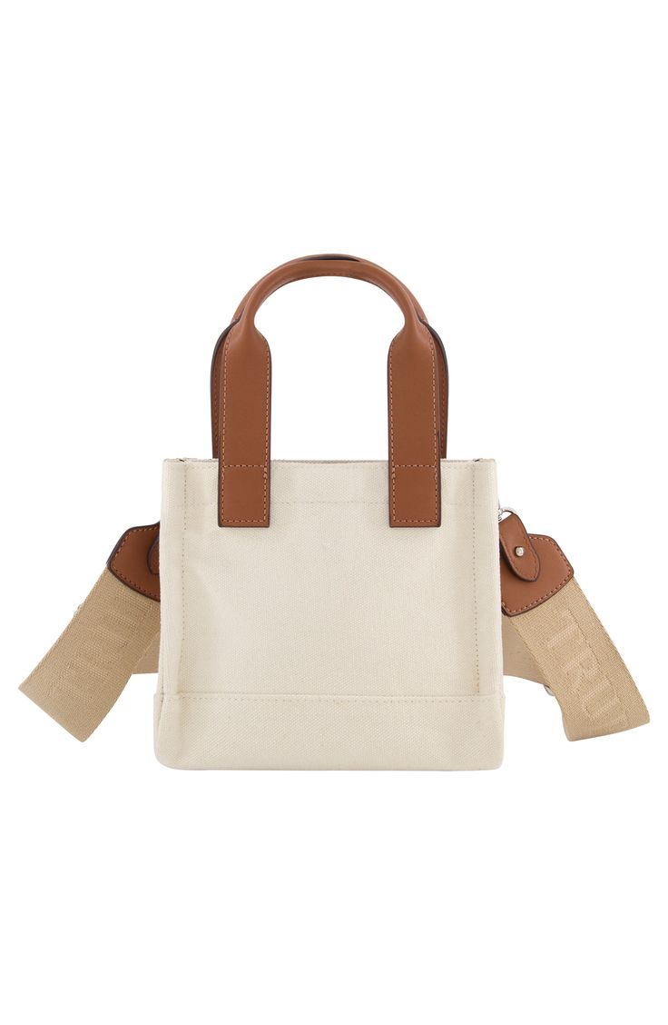 The oversized logo stamps a signature finish on a squared mini tote bag with leatherette top handles to comfortably weekend essentials in style. 18" H x 7" W x 4" D Magnetic top closure Exterior has front snap pocket Cotton/polyester with faux leather trim Lined Imported Trendy Beige Box Bag With Top Carry Handle, Square Beige Shoulder Bag For Daily Use, Casual Square Bag With Leather Handles, Canvas Satchel Bag With Adjustable Handle For Shopping, Trendy Canvas Satchel With Handles, Cream Satchel With Adjustable Handle For Everyday Use, Cream Box Bag With Top Carry Handle For Travel, Trendy Canvas Satchel For On-the-go, Adjustable Handle Satchel Canvas Bag For Shopping