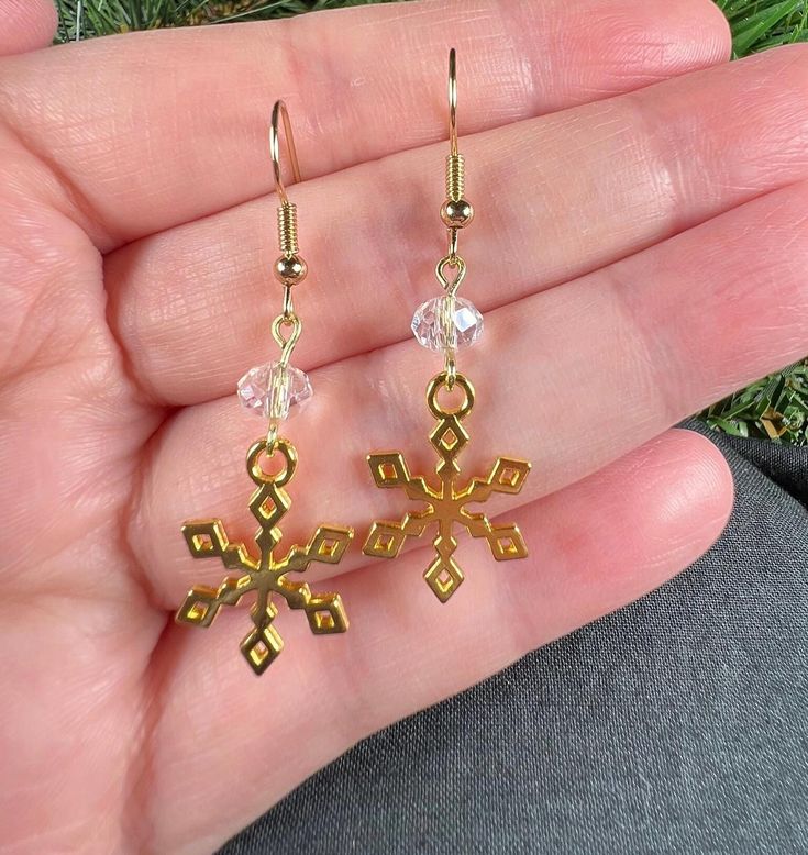 This is a pair of gold toned fish hook dangle earrings.  They feature a gold snowflake charm with a clear faceted glass bead.  They have a 2 inch drop length. Elegant Gold Earrings For Winter, Gold Earrings For Winter Holiday, Gold Earrings For Holiday Season, Holiday Gold Earrings With Ear Wire, Gold Dangle Earrings For Holiday, Gold Drop Earrings For Christmas, Gold Earrings With Ear Wire For Holidays, Gold Snowflake Earrings For Gifts, Gold Earrings As Winter Gift