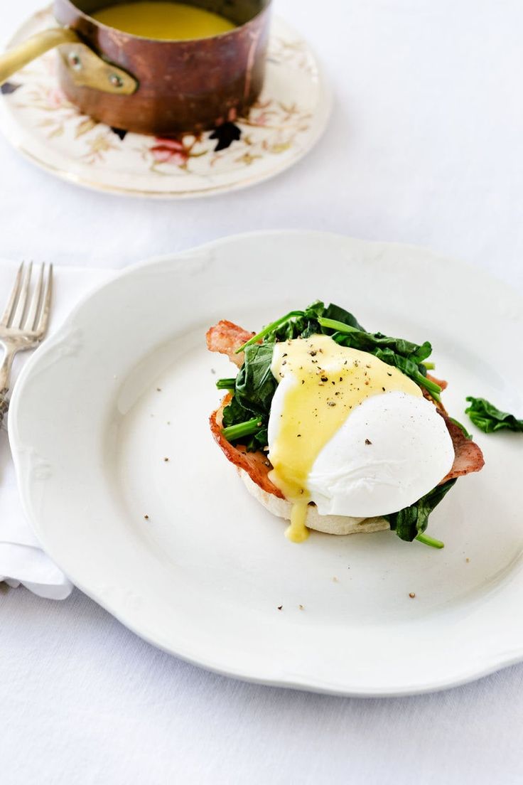 a white plate topped with an egg on top of spinach next to a cup of tea