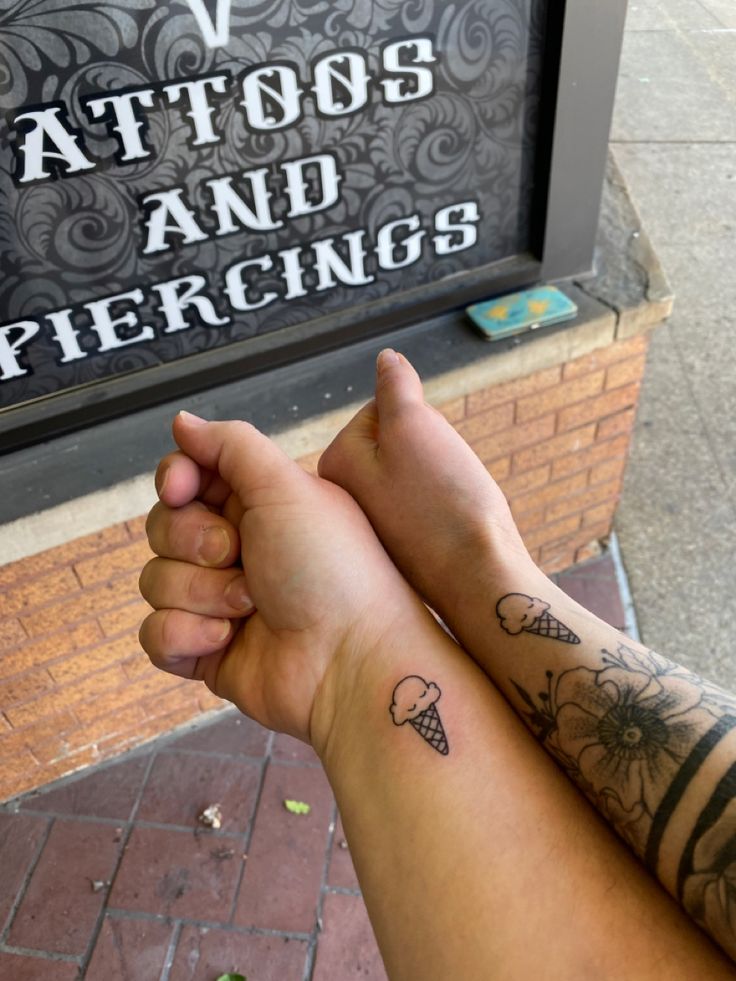 two people holding hands with tattoos and piercings on their arms, in front of a sign