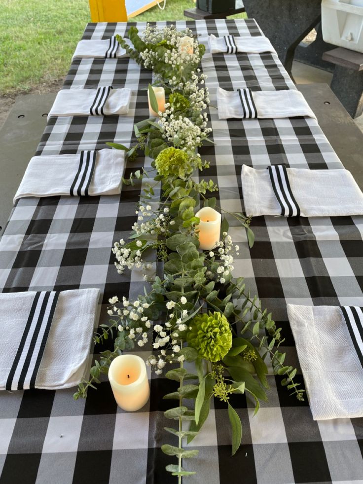 the table is set with black and white checkered cloths, candles, and greenery