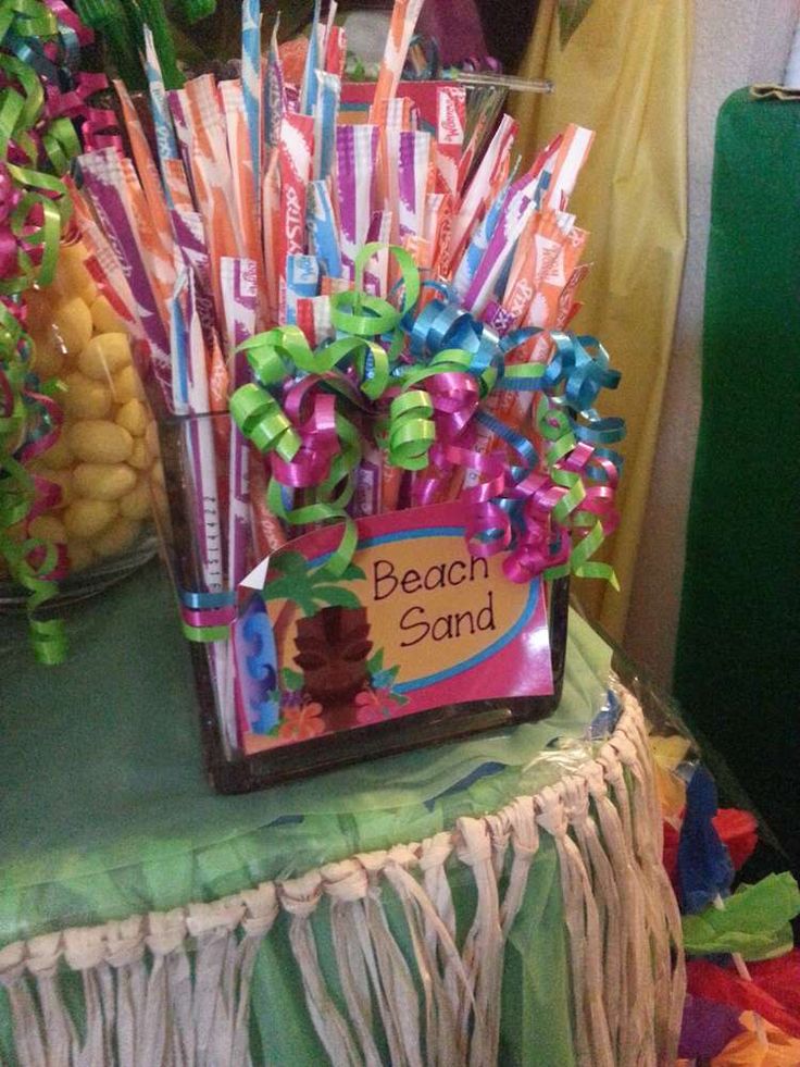 there is a beach sand sign on the table with candy sticks in it and other decorations around it