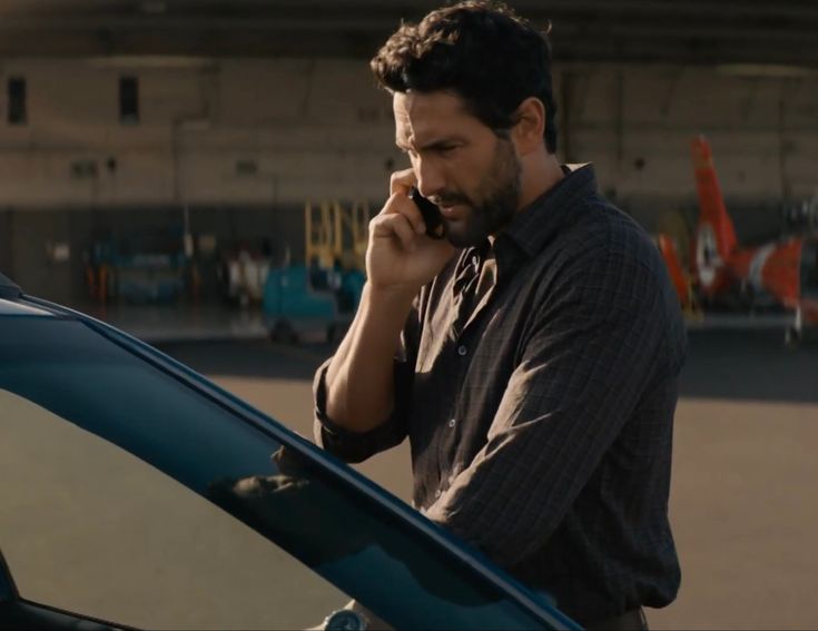 a man standing next to a car talking on a cell phone