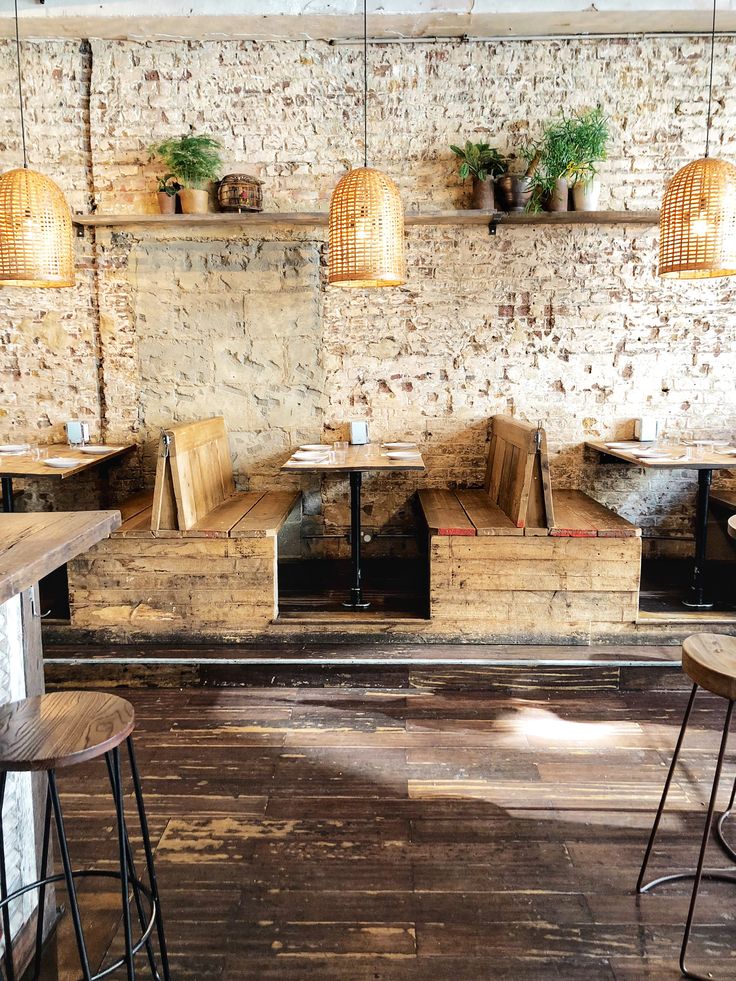 the interior of a restaurant with wooden tables and stools in front of a brick wall