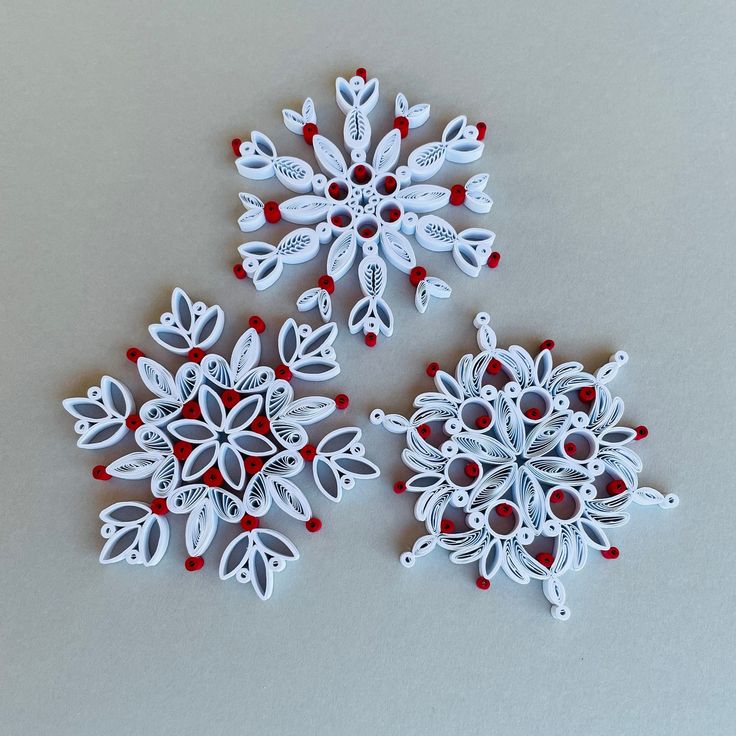 three white snowflakes with red and white decorations on the top one is made out of paper