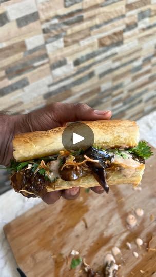 a person is holding a sandwich with mushrooms and lettuce on it in front of a stone wall