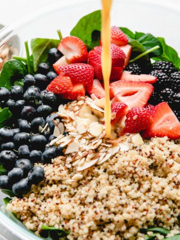 strawberries, blueberries, and spinach are being poured into a bowl