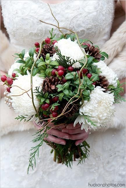 a bridal holding a bouquet of white flowers and greenery with pine cones on it