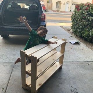 a young boy standing next to a wooden box on the sidewalk with his hand up in the air