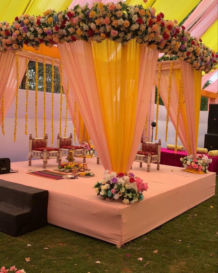 an outdoor wedding setup with flowers on the table and yellow draping over it