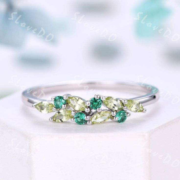 three stone ring with green and white stones on it, sitting on top of a box