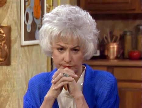 an older woman sitting at a table with food in her hand and looking off to the side