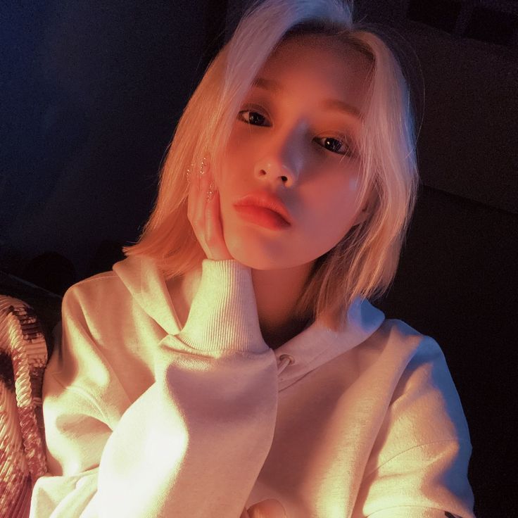 a woman with blonde hair wearing a white sweater and holding her hand on her chin