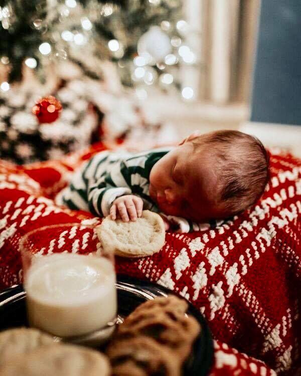 a baby is sleeping on a blanket next to a christmas tree with cookies and milk