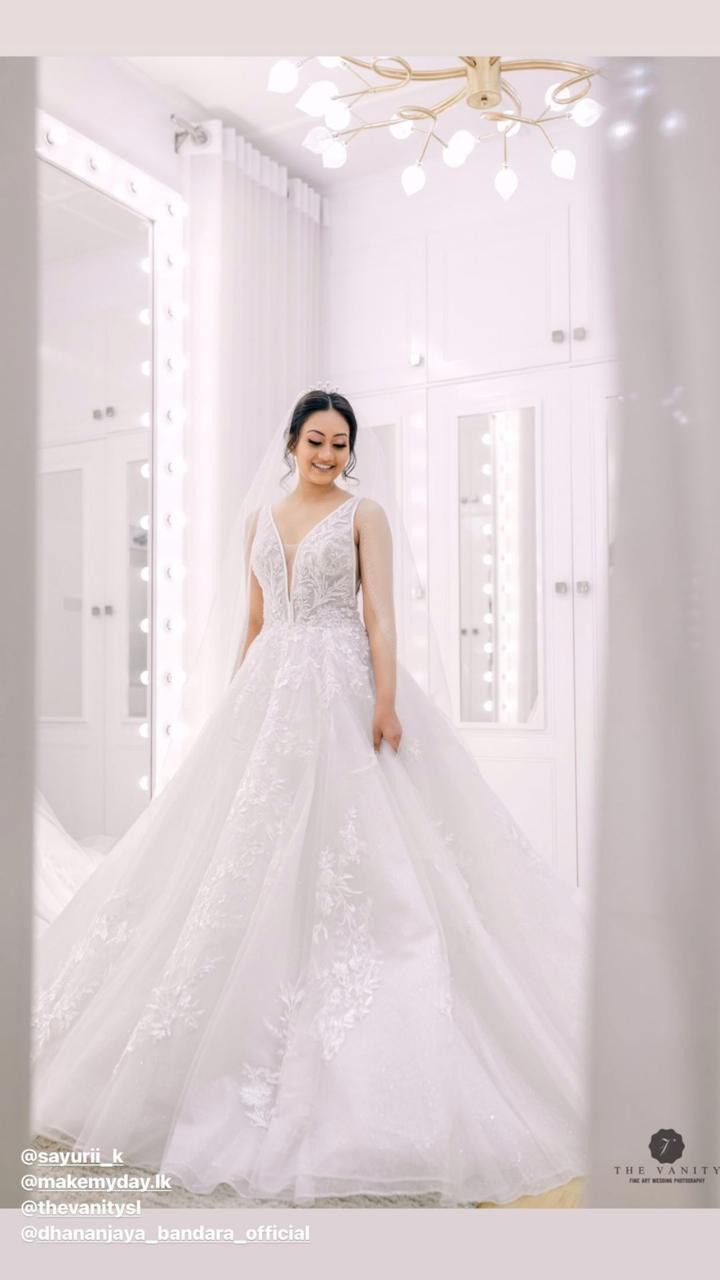 a woman in a white wedding dress standing in front of a mirror with lights on it