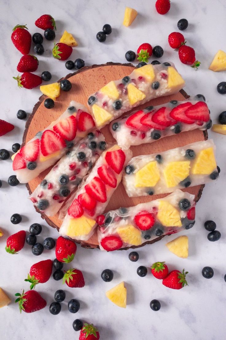 sliced fruit and ice cream on top of a wooden board with berries, pineapples, blueberries, and strawberries