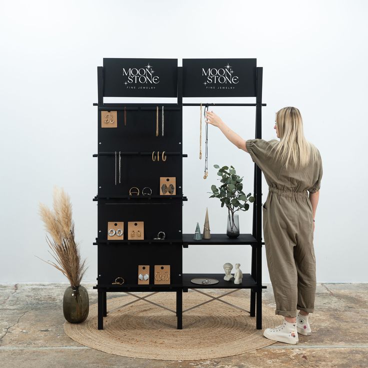 a woman standing in front of a black shelf with earrings on it and a sign that says moon stone