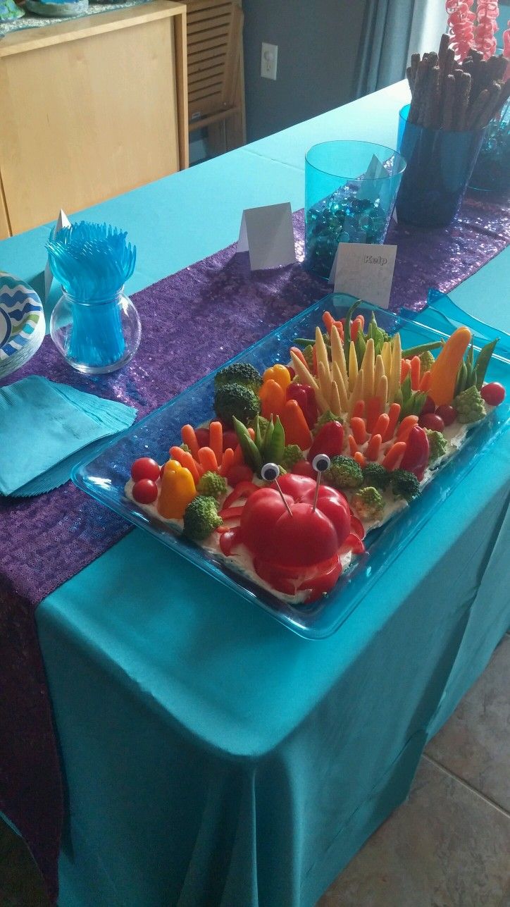 a table topped with a tray of fruit and veggies on top of a blue table cloth