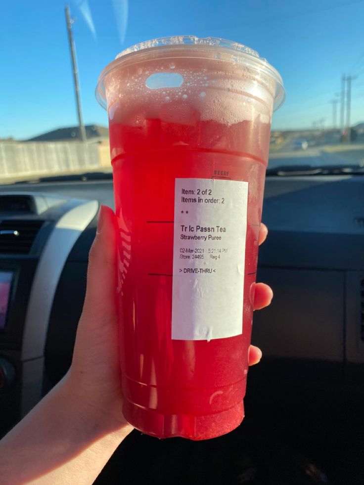 a person holding up a red drink in their hand with a paper label on it