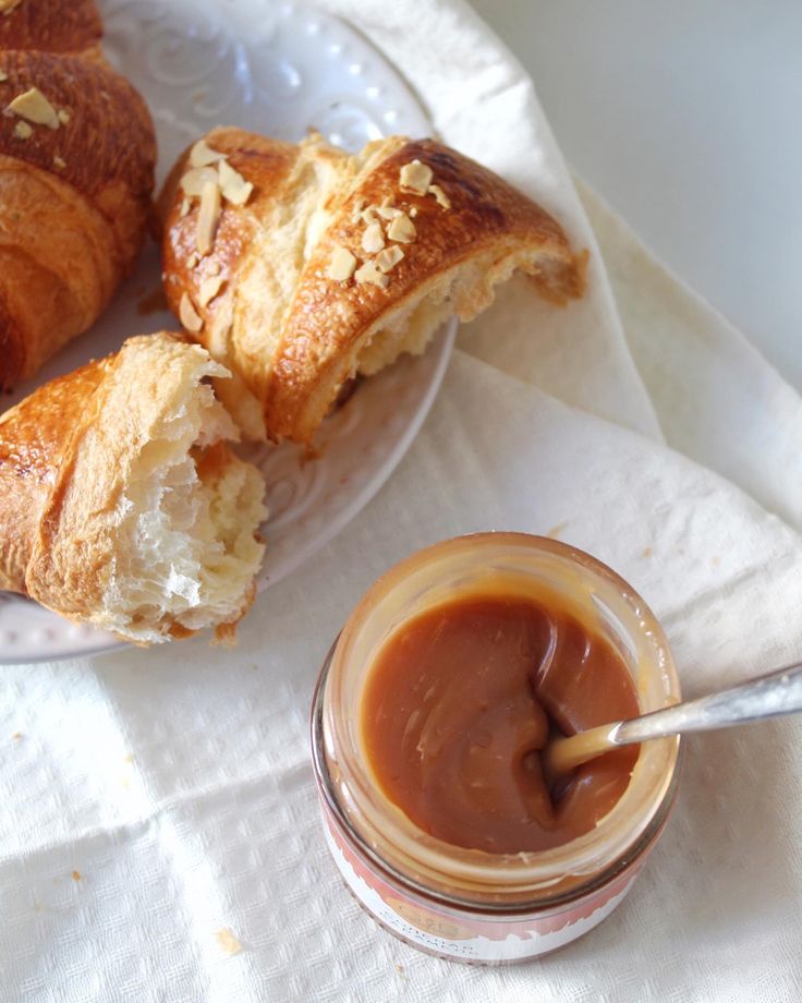 two croissants with peanut butter on the side and a jar of peanut butter