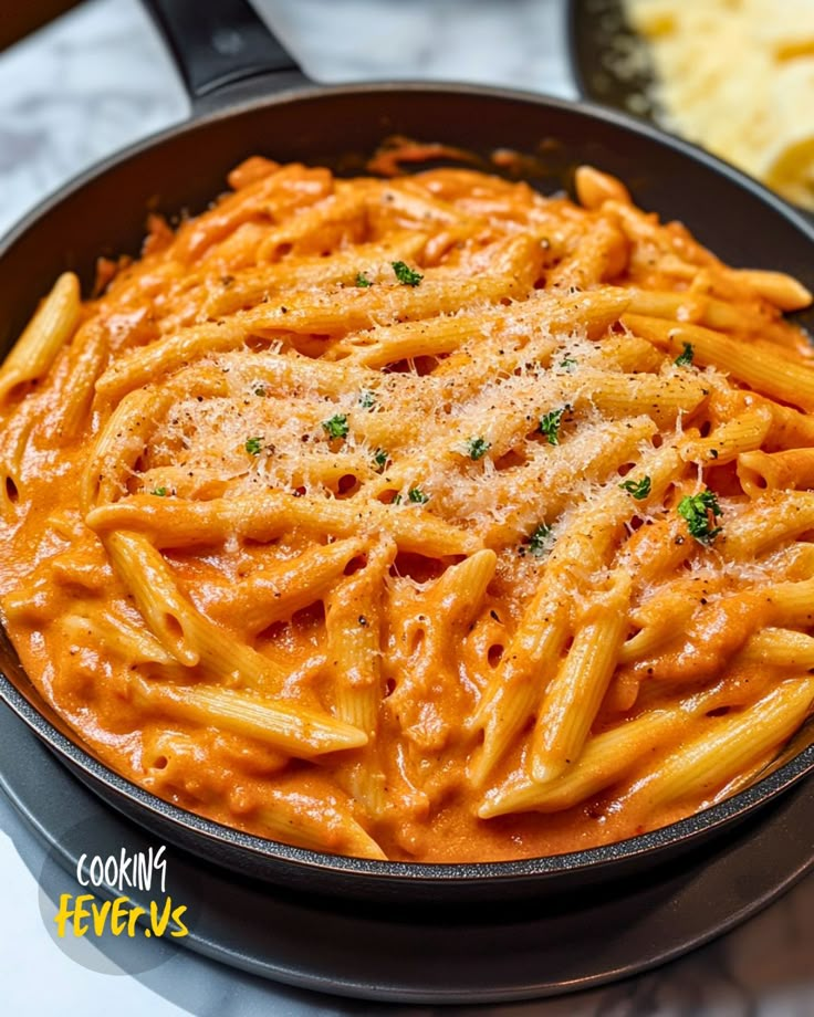 a skillet filled with pasta and sauce on top of a marble counter next to cheese