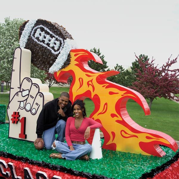 two people posing in front of a fake football field with fire and flames on it