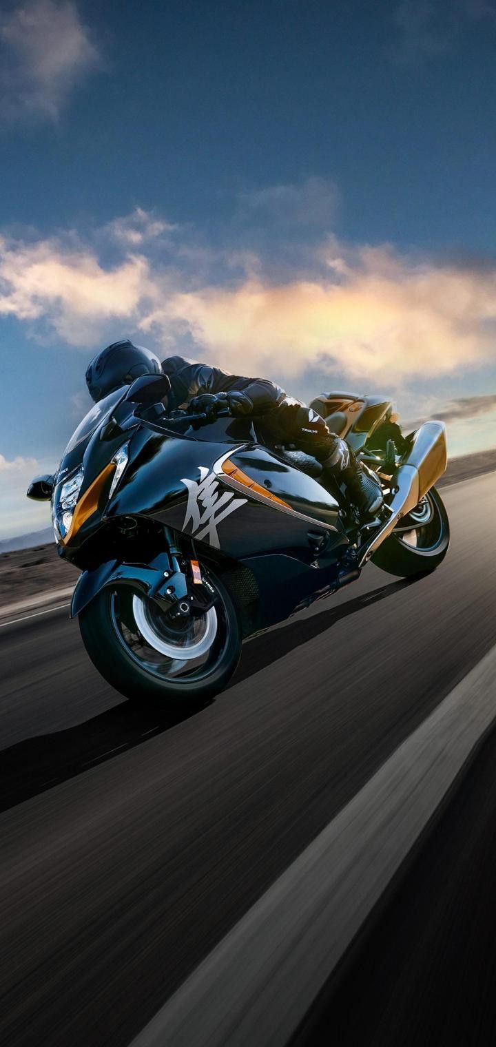 a man riding on the back of a motorcycle down a road in front of clouds