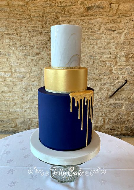 a blue and gold wedding cake with icing dripping from the top on a table