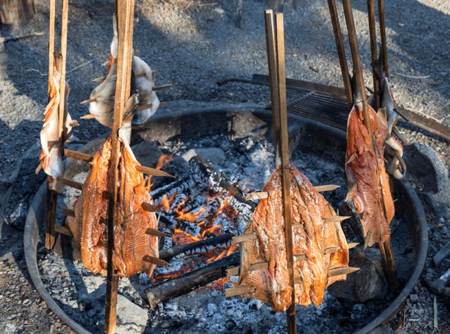 some meat is cooking on the grill in the fire pit with sticks sticking out of it