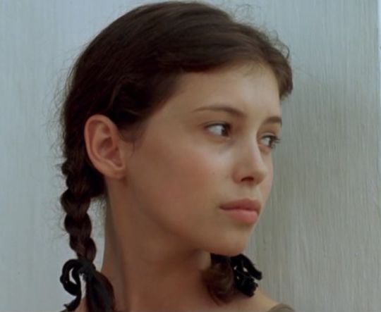 a woman with braids on her hair looking off to the side in front of a white wall