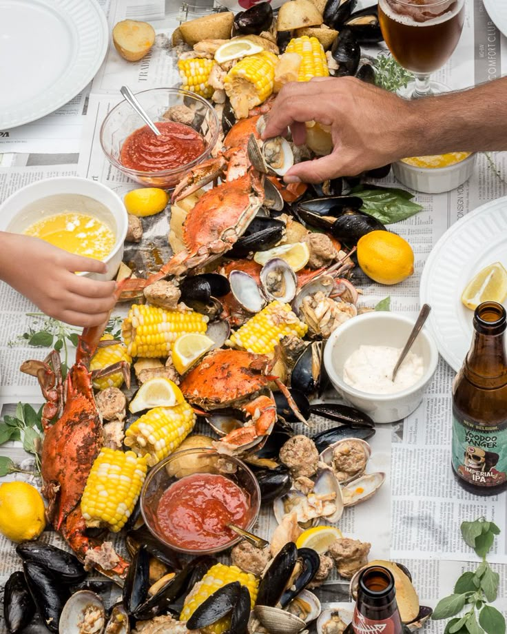 people are eating lobsters and corn on the cob at a table with beer