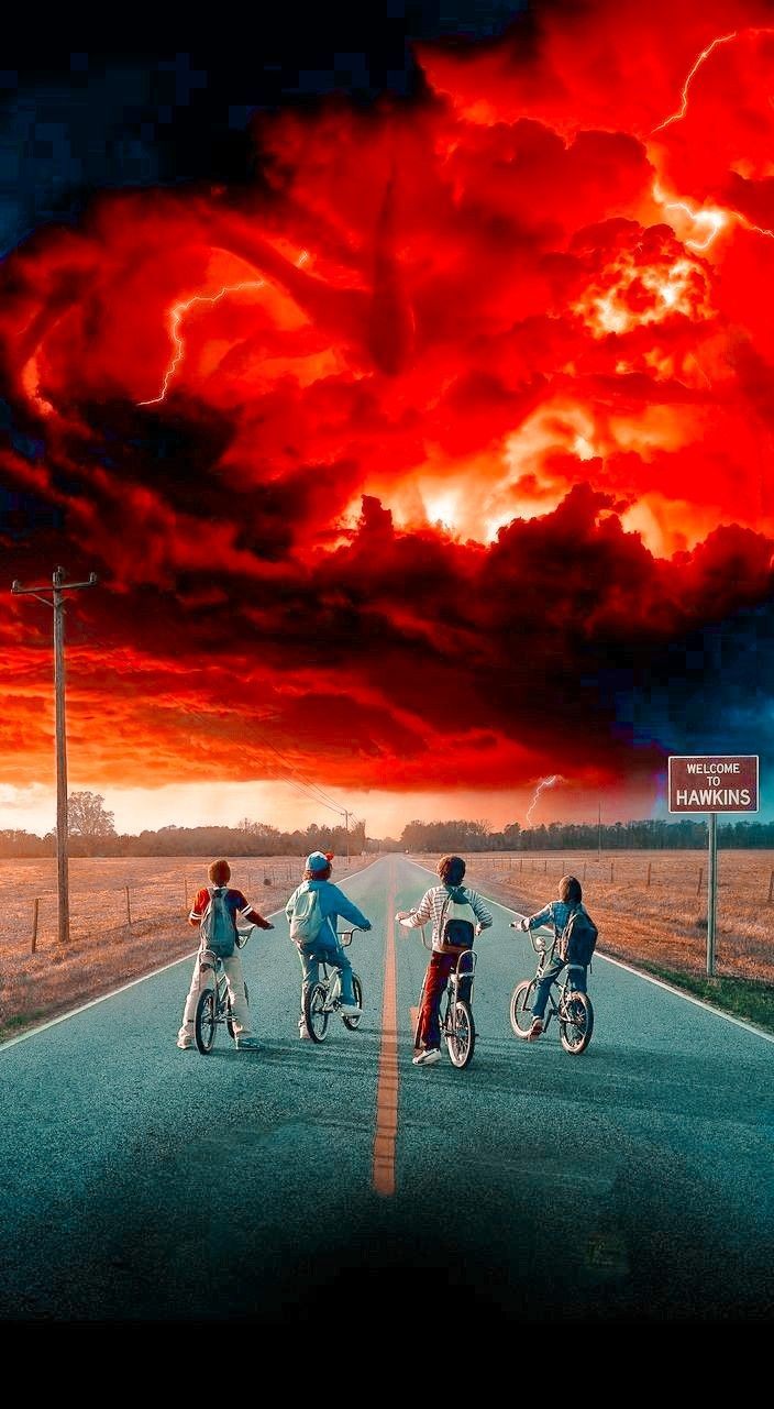 three people riding bikes down the middle of a road under a red cloud filled sky