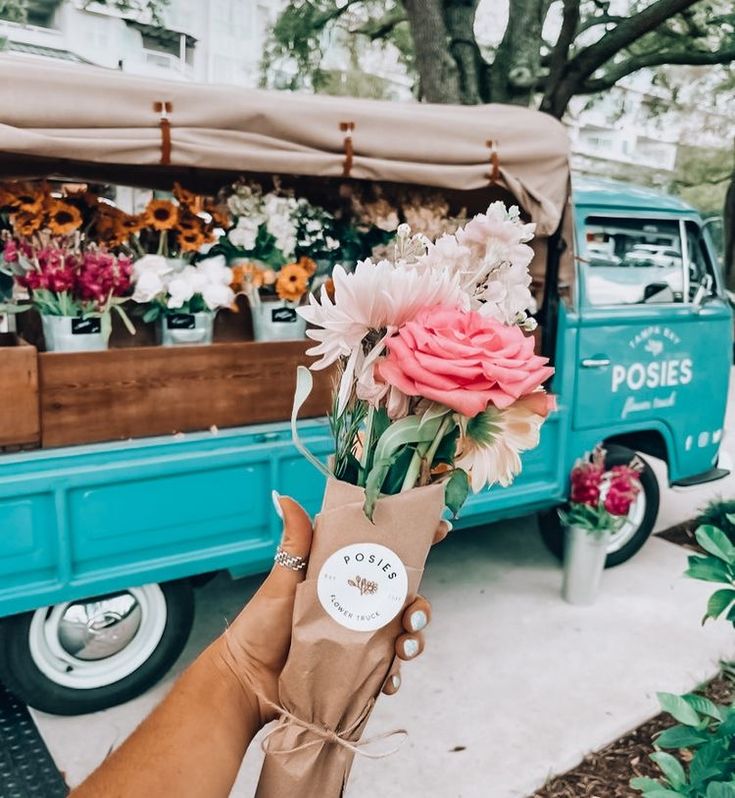 a person holding a bouquet of flowers in front of a blue truck parked on the street