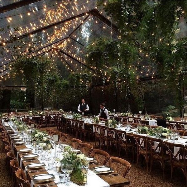 an outdoor wedding reception with string lights and greenery on the ceiling, surrounded by wooden chairs